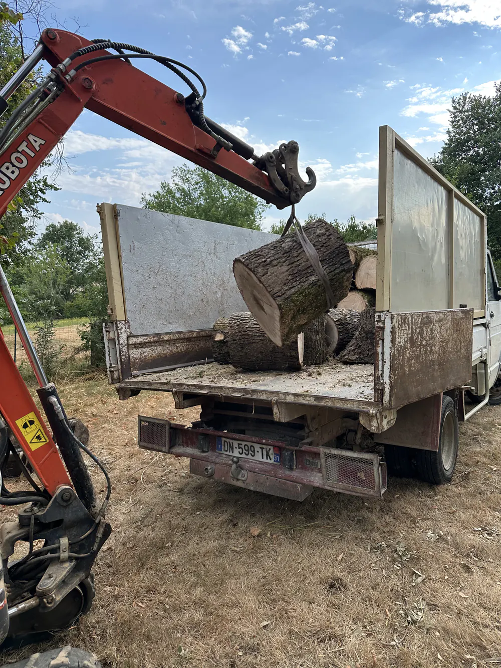 Tronçons de bois chargés dans un camion à l'aide d'une mini-pelle